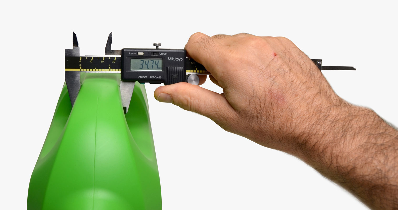 Hand measuring the depth of a green plastic bottle with measurement tool